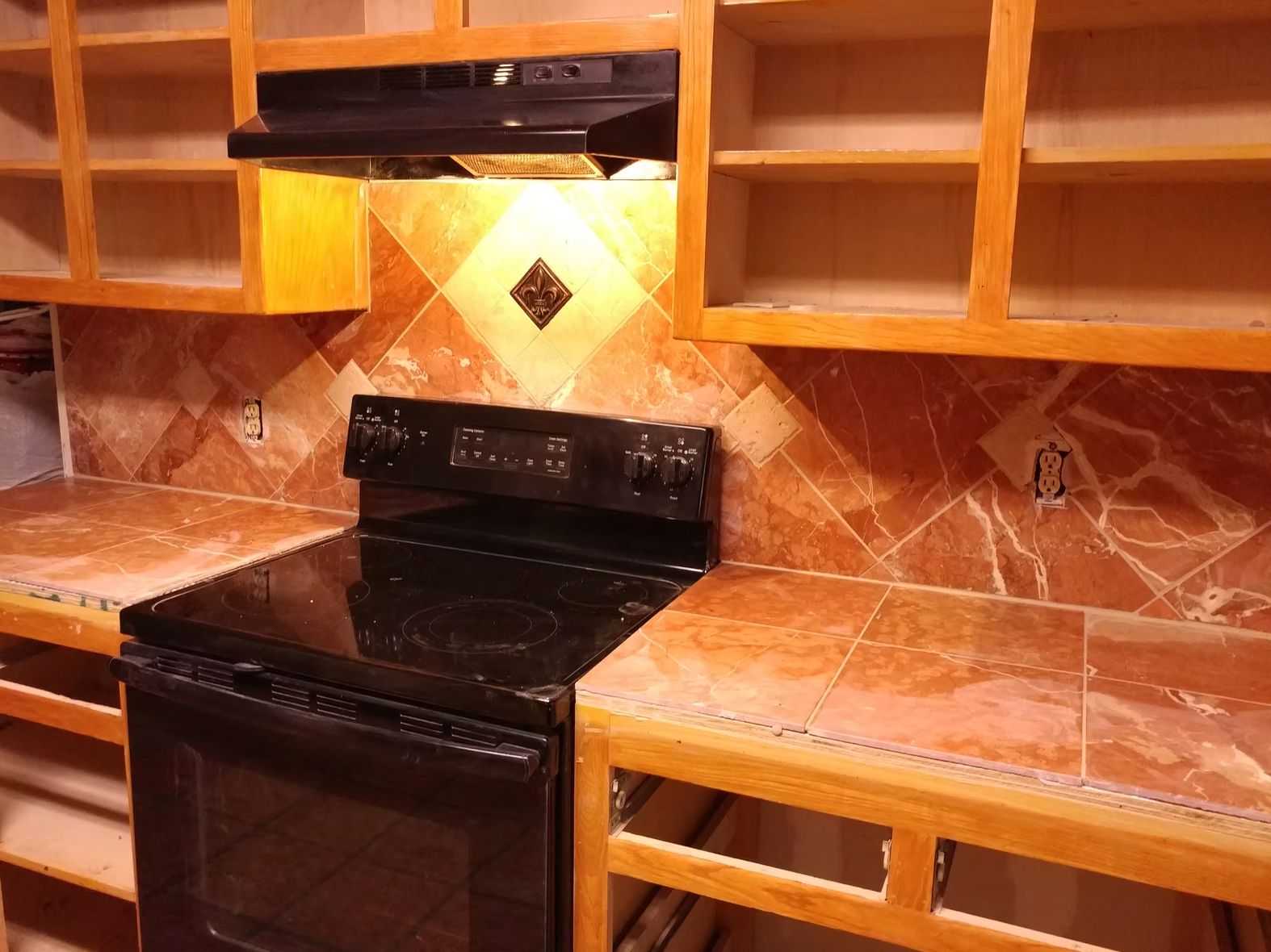 Modern kitchen with black electric range, orange tile backsplash, wood cabinets with glass doors, and range hood