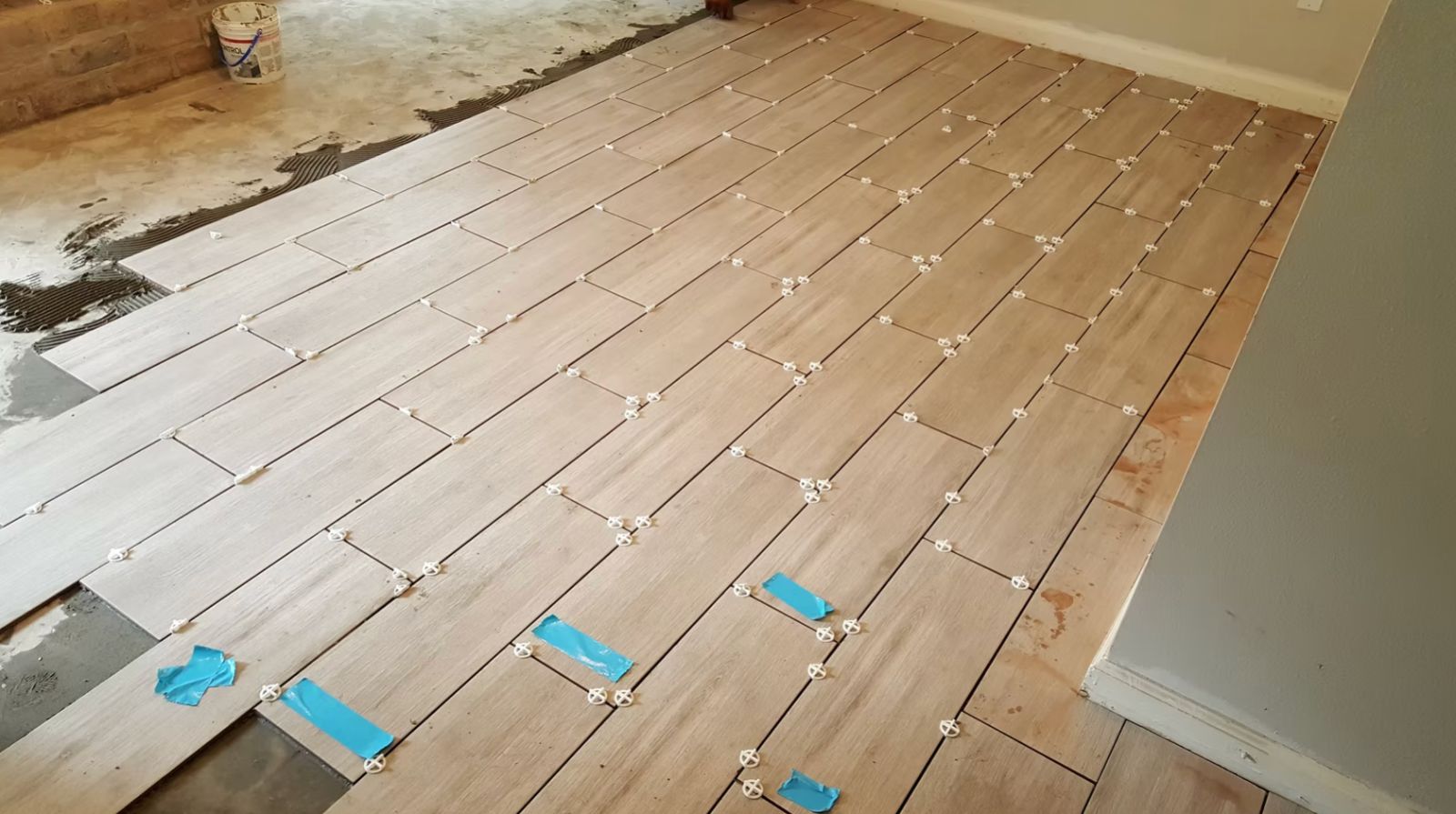 Luxury vinyl plank flooring installation in progress with spacers and adhesive on concrete subfloor