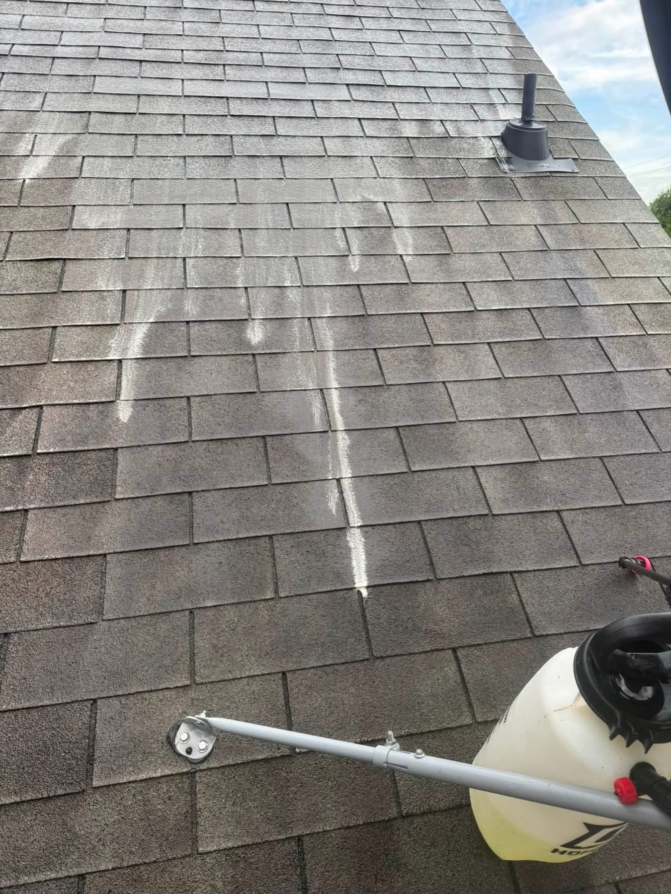 Roof cleaning with pressure washer on asphalt shingles, white stream visible