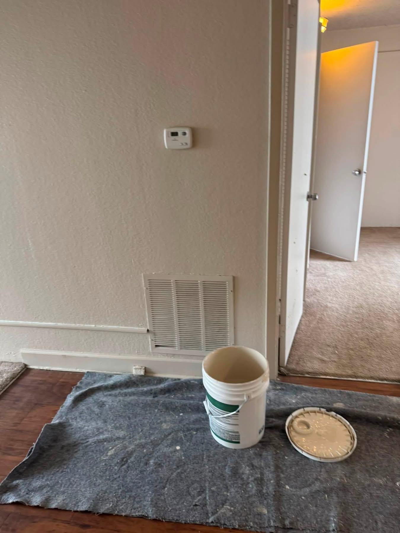 Interior room with paint bucket, pie tin, and drop cloth on hardwood floor