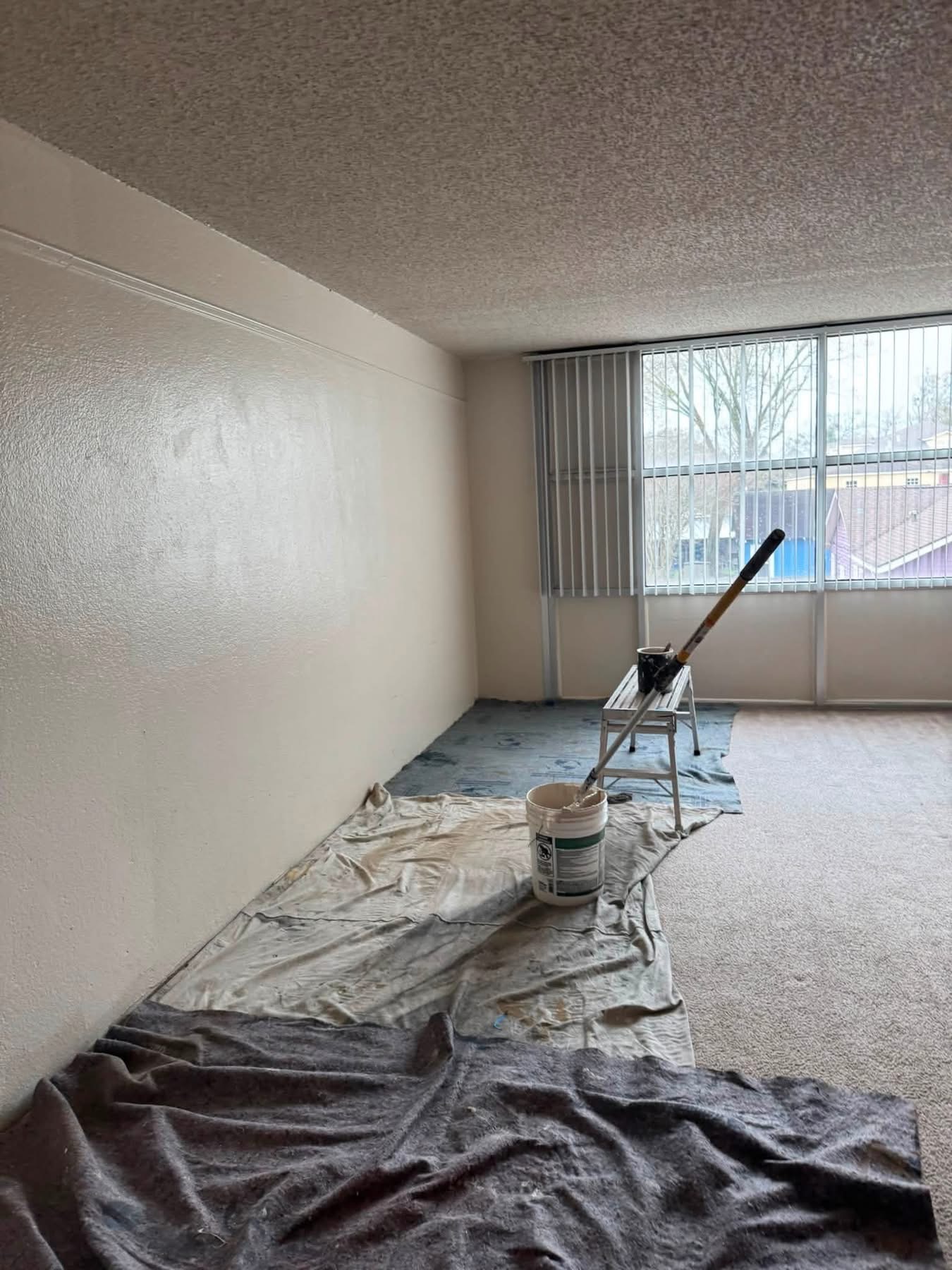 Interior room under renovation with paint bucket, roller tool, and drop cloths covering floor