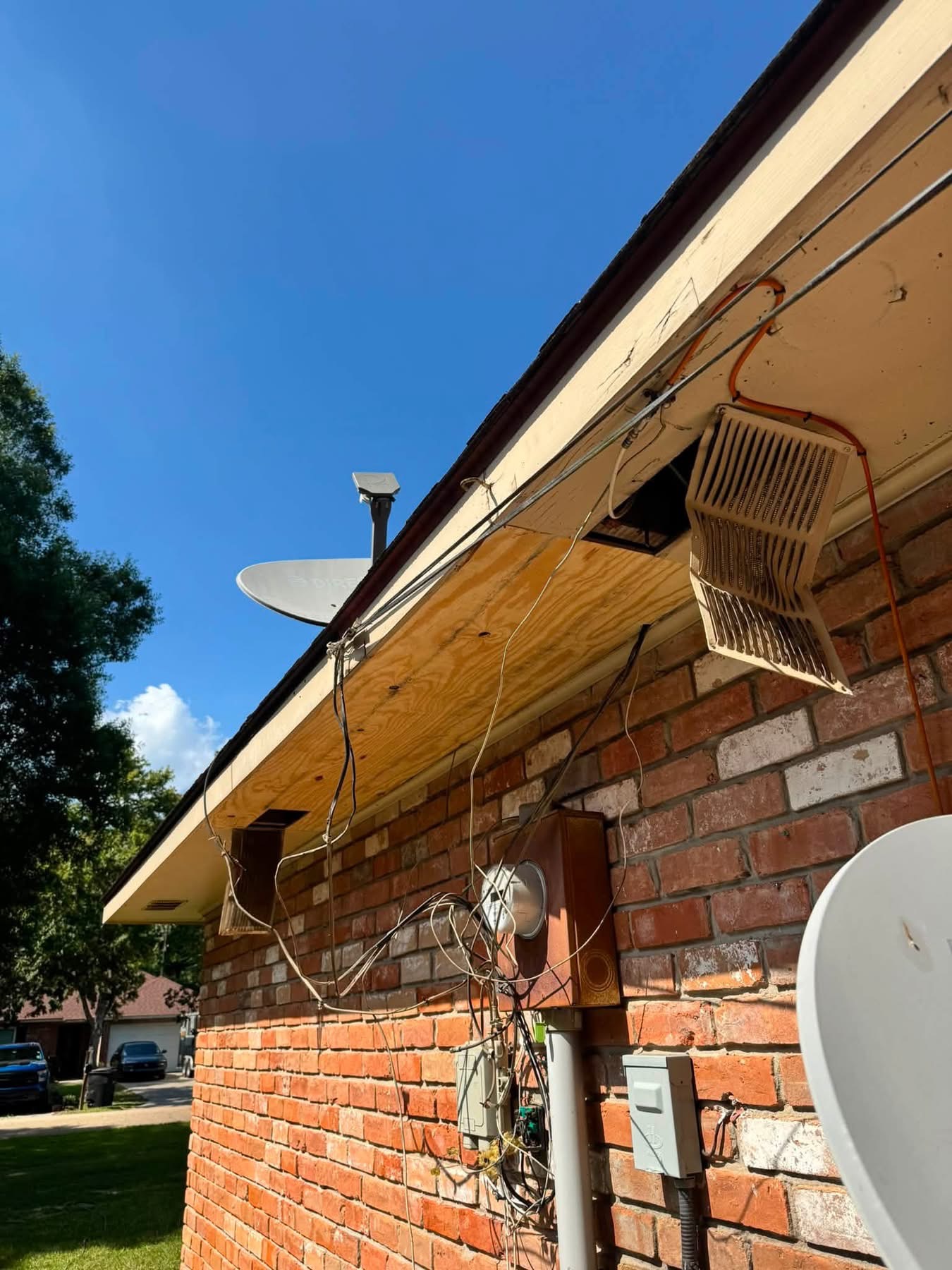 Satellite dishes and wiring mounted on brick house exterior with clear blue sky