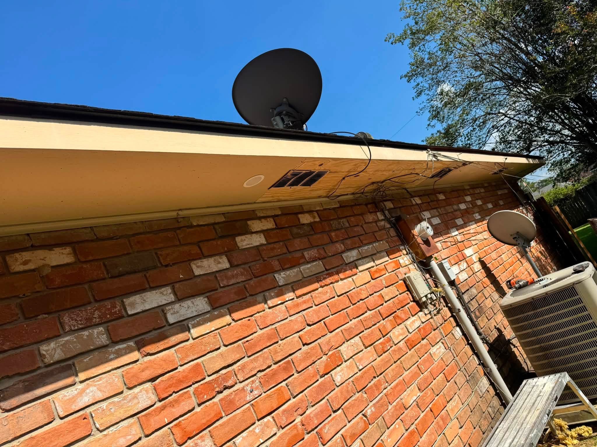 Satellite dish mounted on tan roof trim above red brick residential building wall