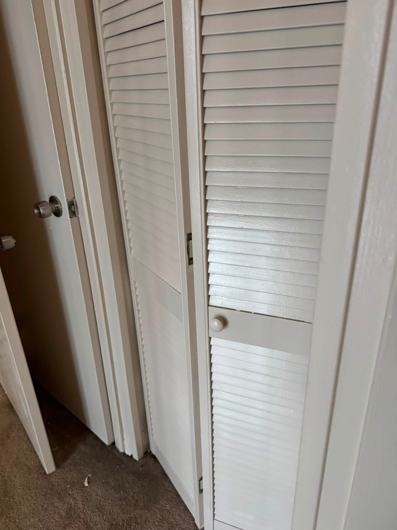White louvered closet doors with metal hardware in an open position