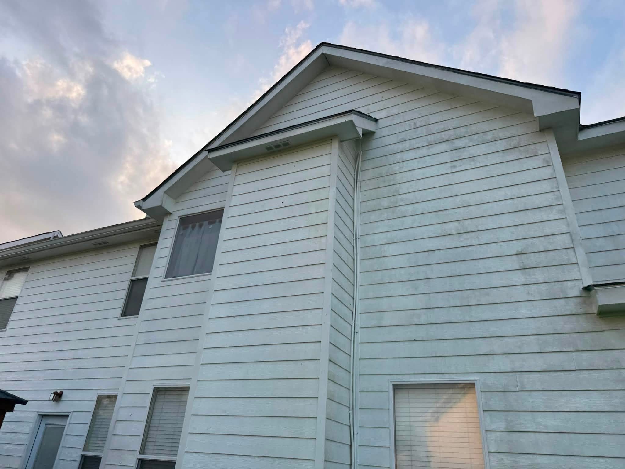 White vinyl-sided two-story residential house with gabled roof and multiple windows against cloudy sky