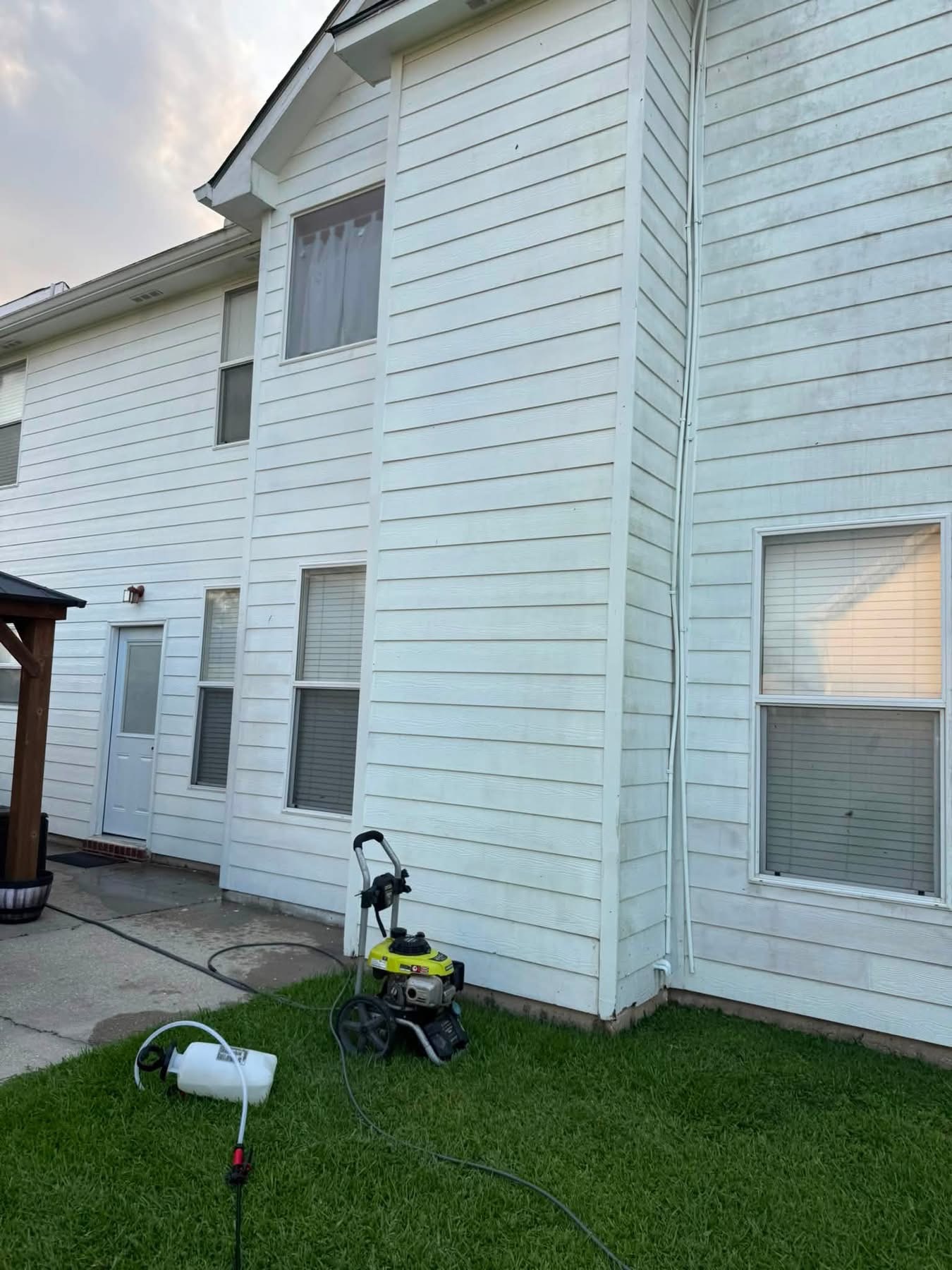 White siding home with pressure washer equipment and hose on grass