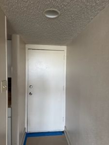 Small white entry door in narrow hallway with blue floor mat