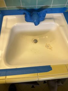 Stained white bathroom sink with blue towel draped over faucet