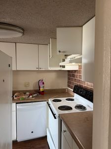 Compact kitchen with white cabinets, electric stove, and beige countertops