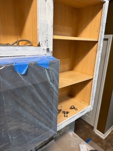 Open wooden cabinet with blue tape on shelf and construction materials visible inside