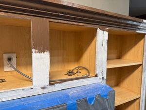 Interior cabinet shelving with blue painter's tape and white protective coverings during renovation work