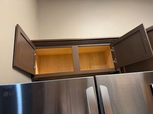Open kitchen cabinet with wooden interior and stainless steel refrigerator below