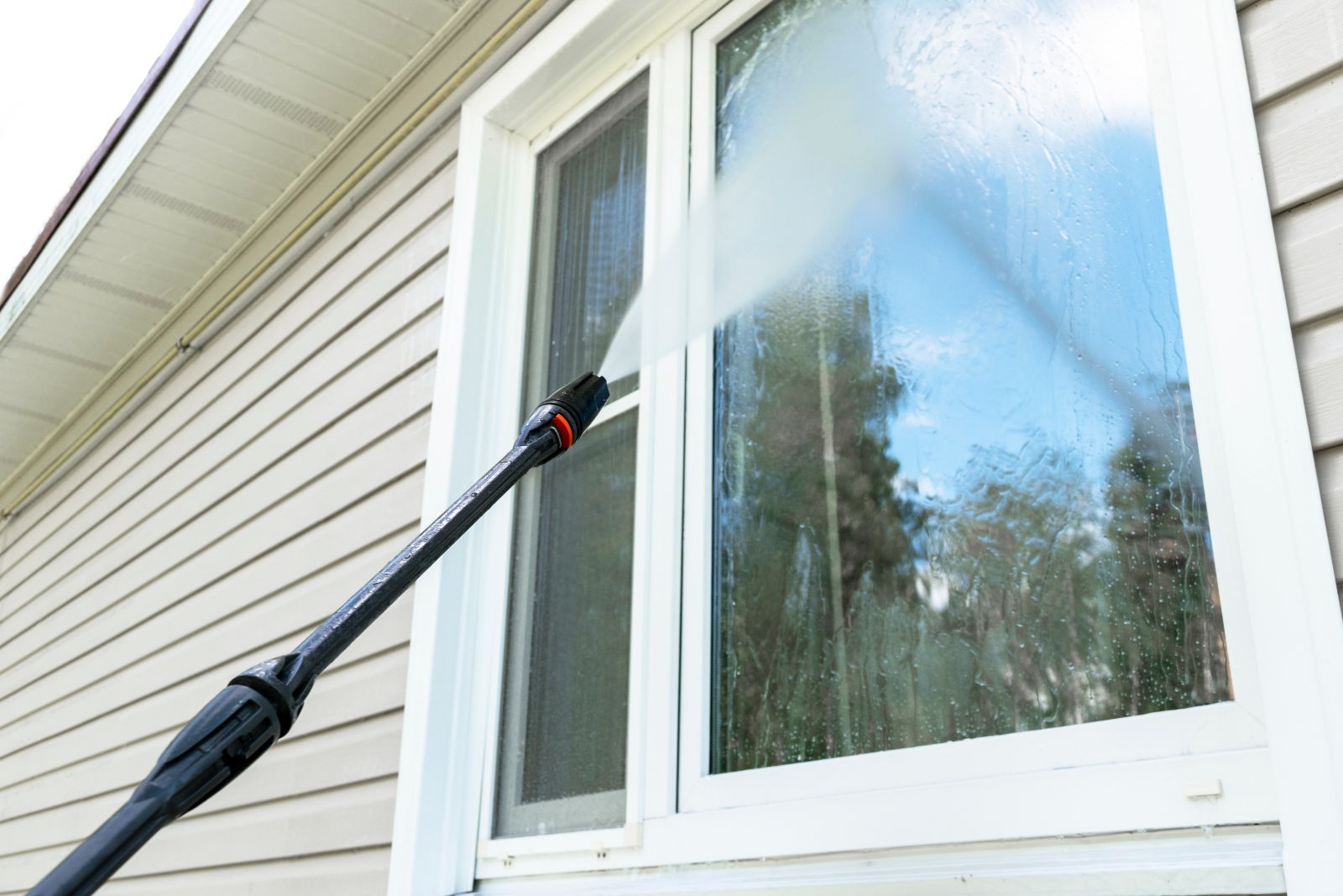 Professional window cleaning with pressure washer on residential home exterior