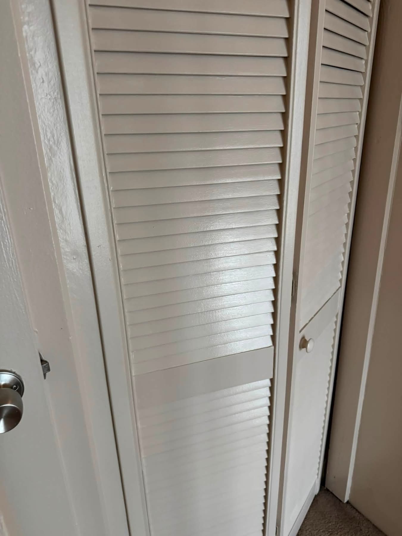 White louvered closet doors in hallway with wall and door frame visible